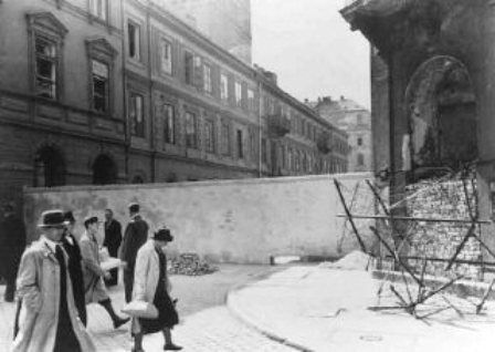 Polish civilians walk by a section of the wall that separated the Warsaw ghetto from the rest of the city. Warsaw, Poland, 1940-1941